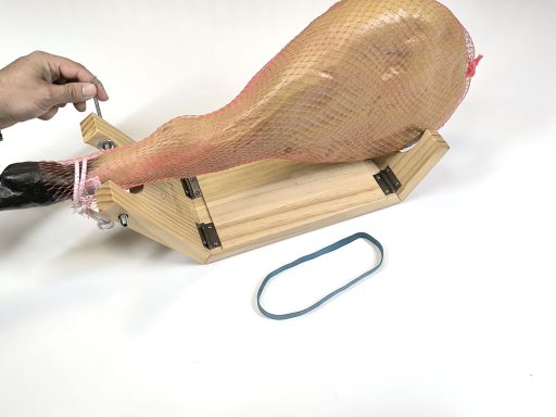 Ajuste del jamón en el Kampé Una pierna de jamón sobre un soporte, con una mano sujetándola y una banda elástica al lado.